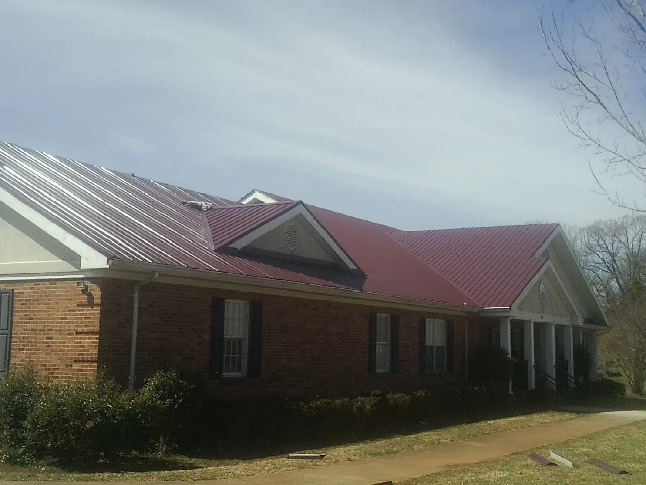 Red metal roof with gabled entries on a long brick building, from a Hail Damage Roof Repair job in Homeland