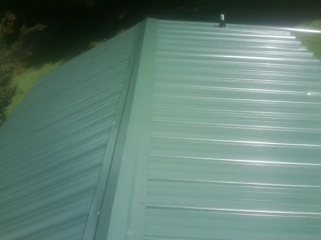 New green metal panels meeting at the ridge of a roof — Flat Roof Repair work by our crew in Homeland