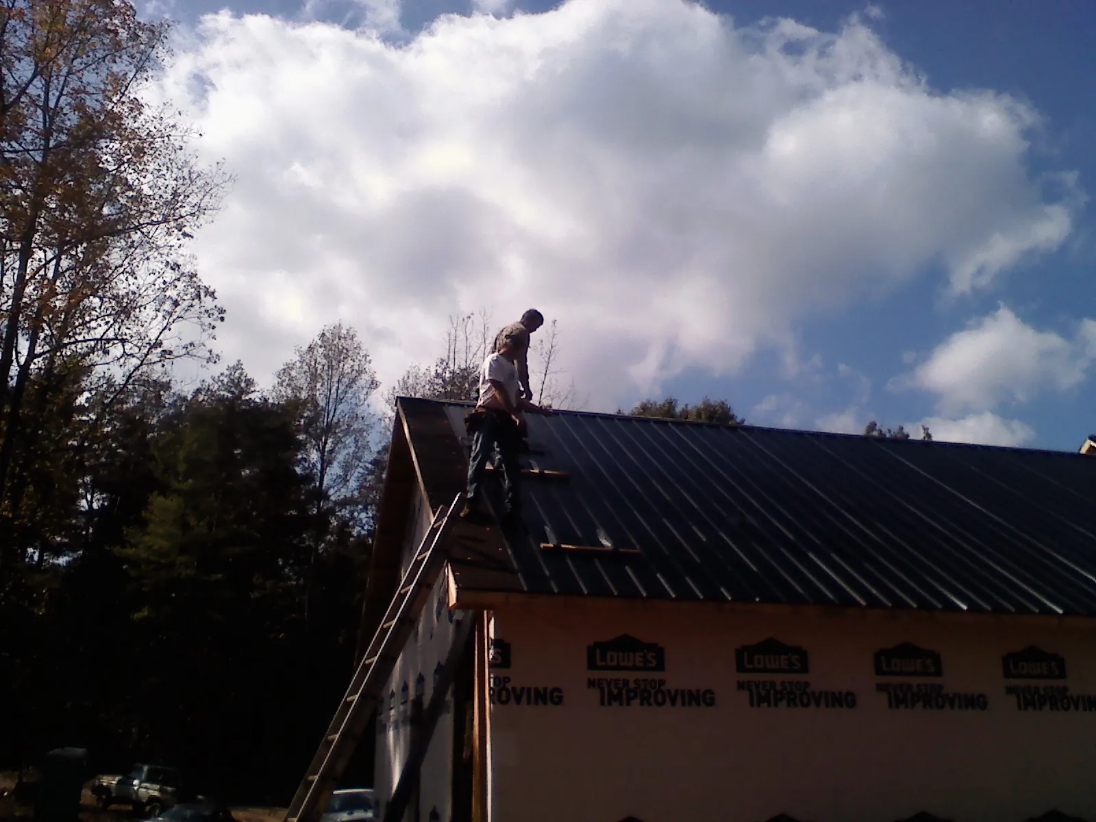 Roofer fastening dark metal panels high against a cloudy sky, from a Roof Inspection job in Homeland