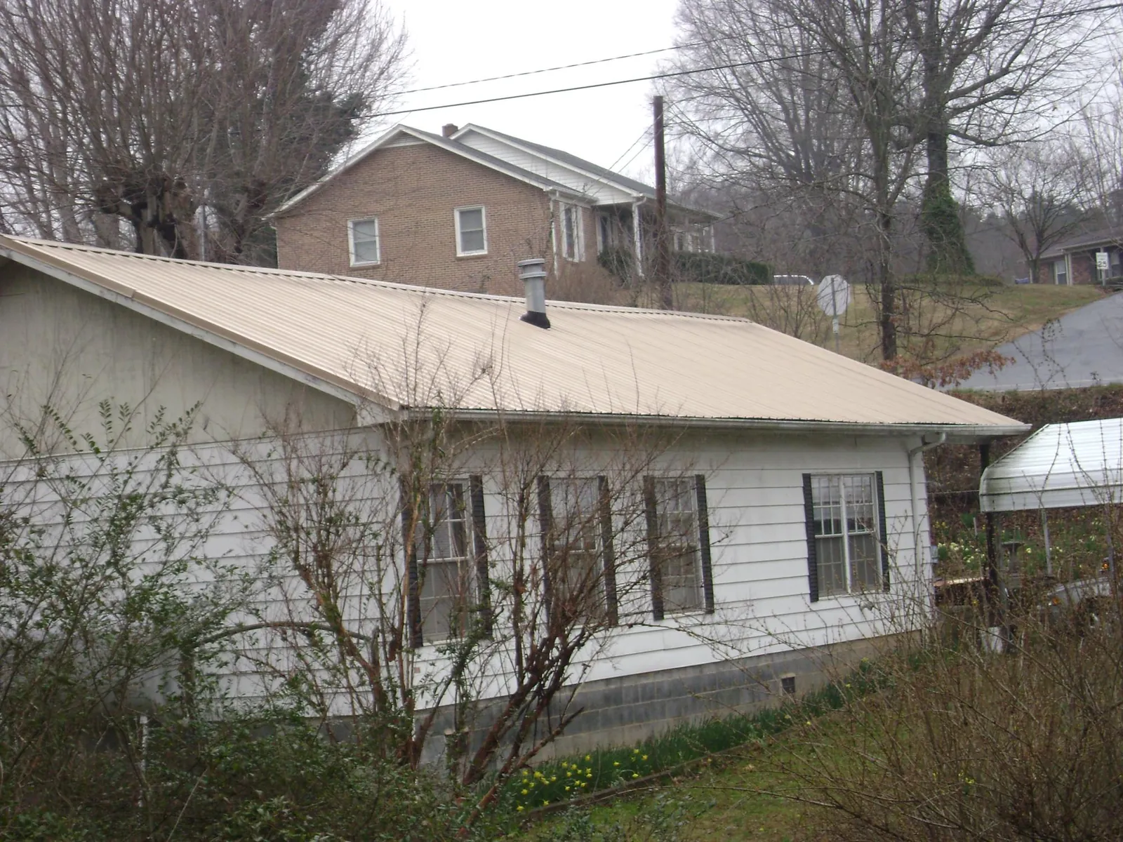 Tan metal roof on a white sided house set into a hillside — Commercial Roofing by Roofing Brothers in Homeland