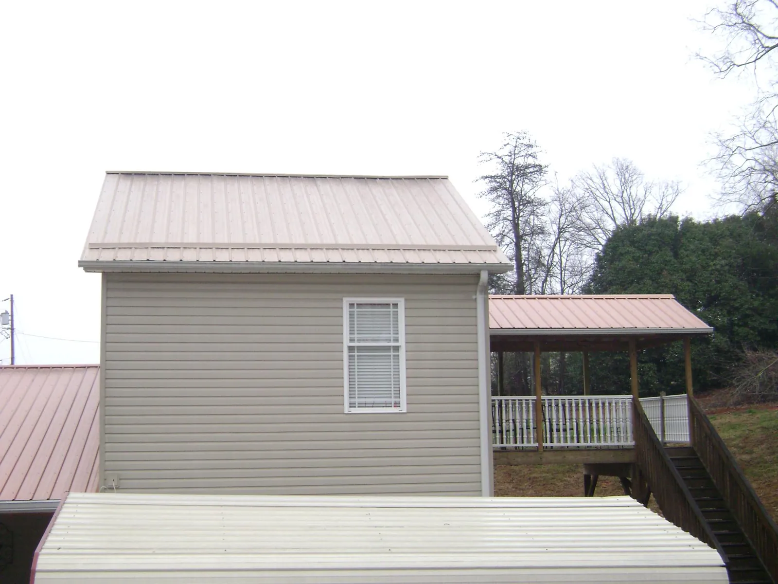 Tan metal roofs on a two story addition and attached porch, from a Roof Replacement job in Homeland